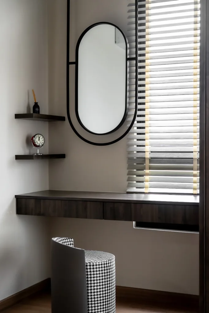 Modern dark vanity with oval mirror, floating shelves, and houndstooth chair.