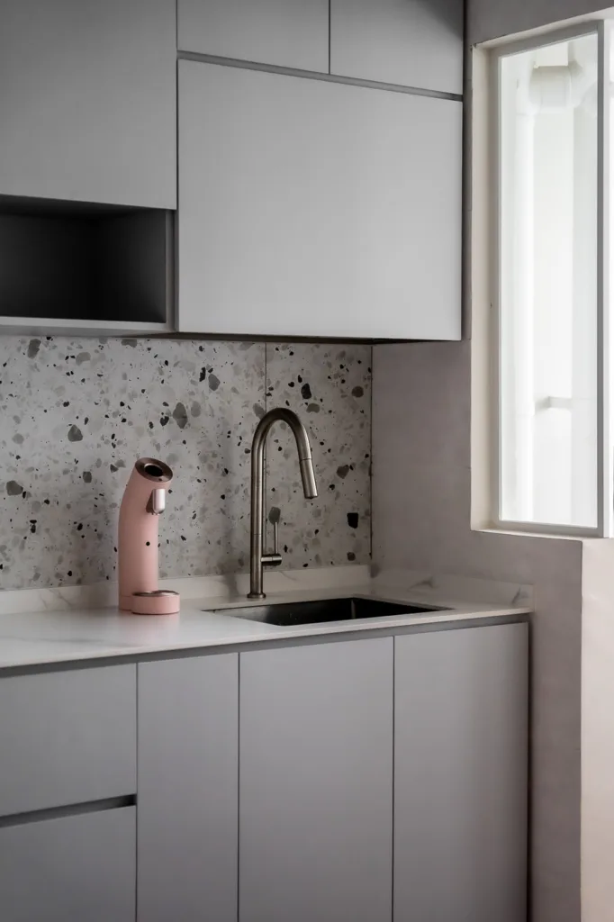 Modern kitchen with gray cabinets, terrazzo backsplash, and a pink water dispenser.