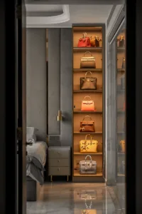a modern room with a bed and a nightstand on the left, featuring a well organized display of various luxurious handbags on illuminated shelves on the right.