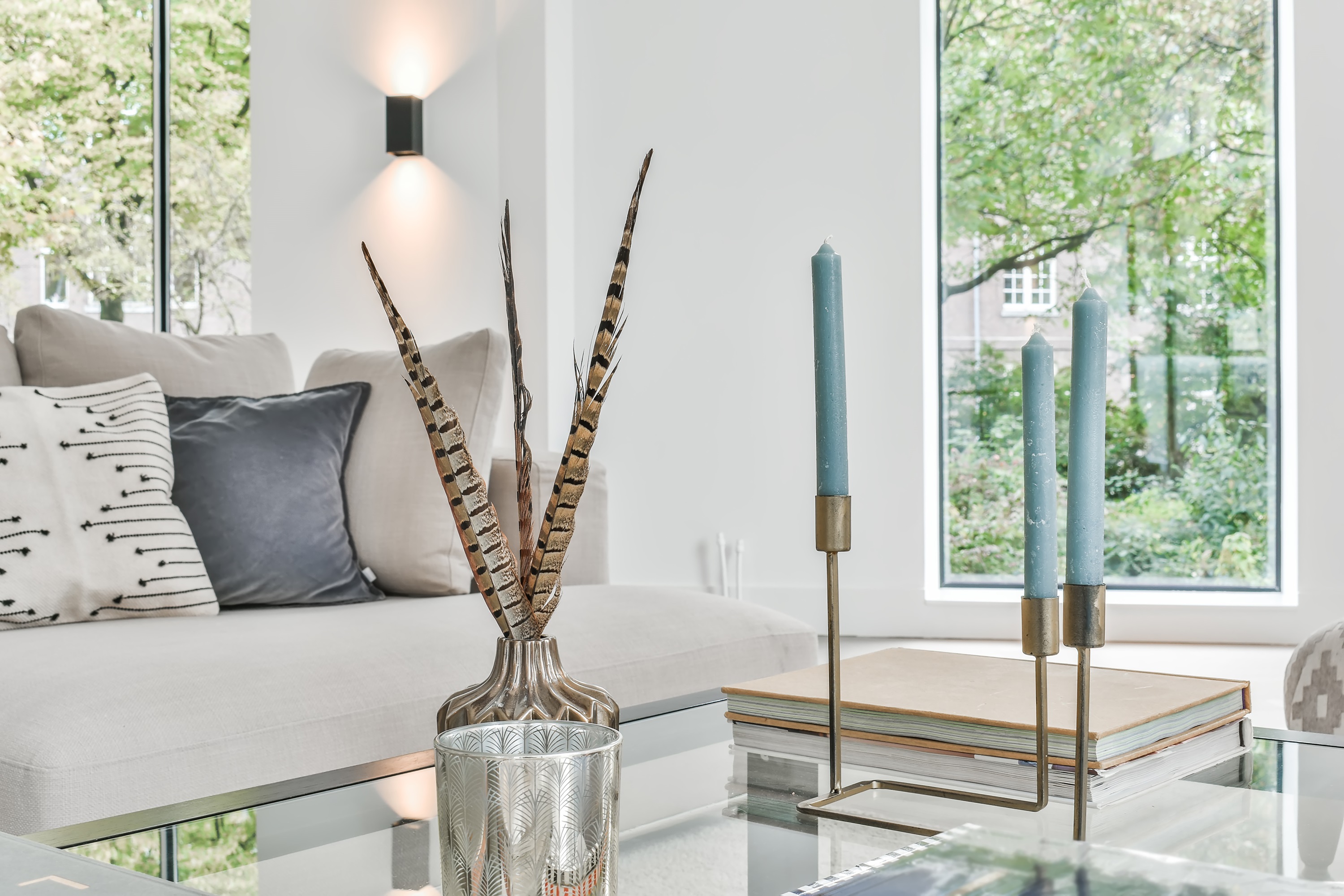 Contemporary living room with glass coffee table, candles, and feather decor. Modern interior design.