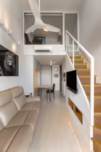 Modern open-plan apartment with loft, stairs, and beige leather sofa.