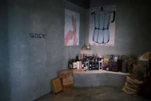 Grey-walled bar with whiskey bottles, coffee poster, and wooden crates.