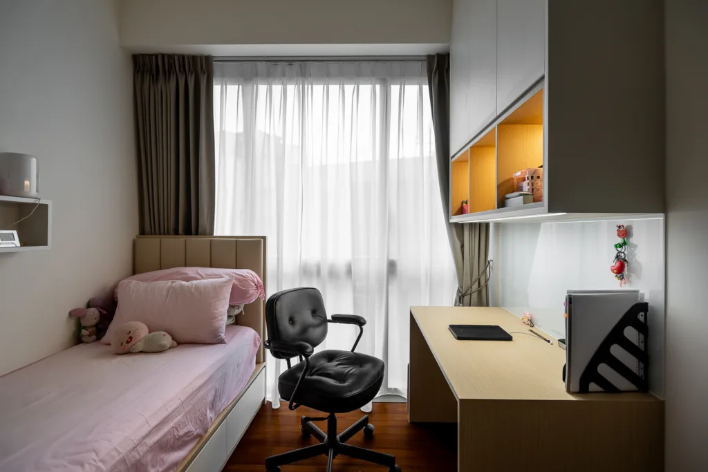 Small bedroom with pink bed, built-in desk, and window. Ideal space saving design.
