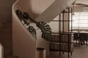 Modern interior with staircase, plant, bookshelf, and dining area.