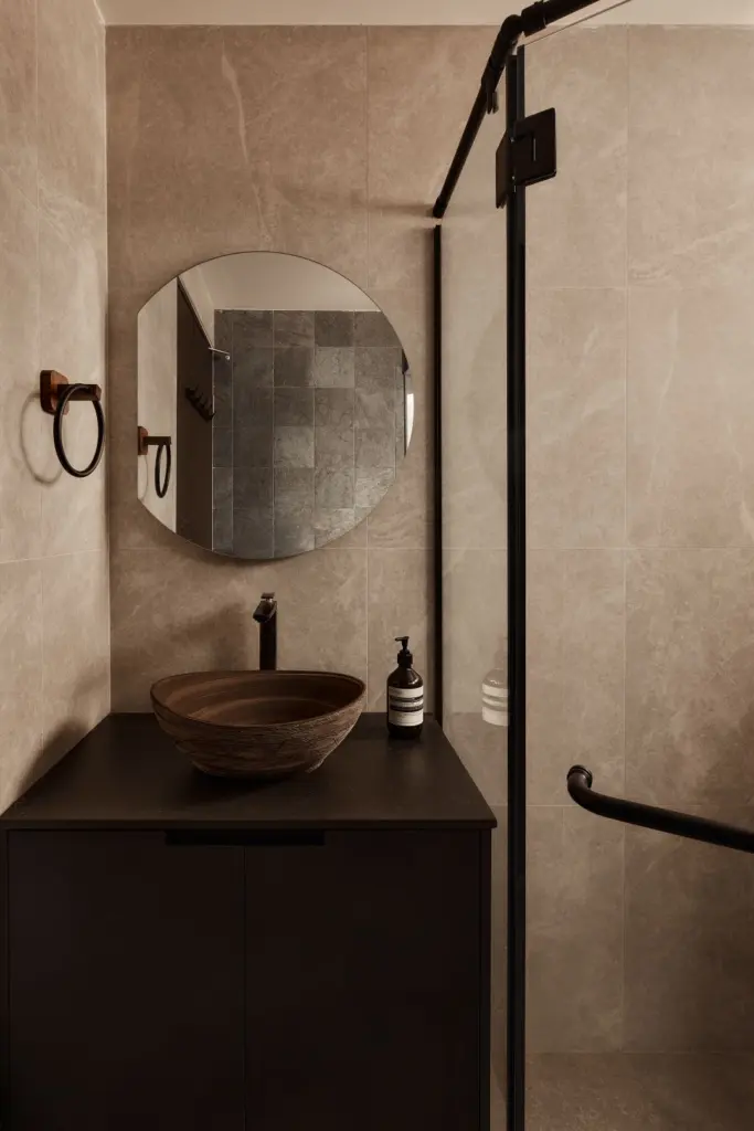 Modern bathroom with round mirror and stone sink.